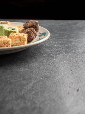 Geleneksel çok renkli oryantal Türk tatlıları (rahat locum) beyaz bir tabakta gri bir zemin üzerinde yatmaktadır. Uzayı kopyala Yan görünüm