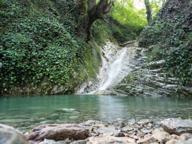 Katmanlı kayalarda güzel, temiz bir şelale hızlı bir derede vaftiz fontuna akar. Şelalenin eteğindeki Aquamarine yazı tipi. Sudaki taşlar, ormanın etrafındaki taşlar. İnsansız dağ manzarası.