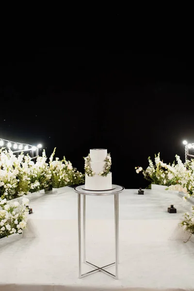 在白色的讲台旁边的一个高看台上摆着绿色装饰的婚礼白色蛋糕 — 图库照片