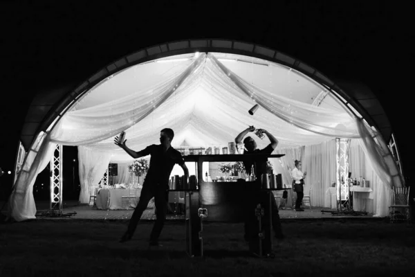show of bartenders against the background of a banquet tent in silhouettes