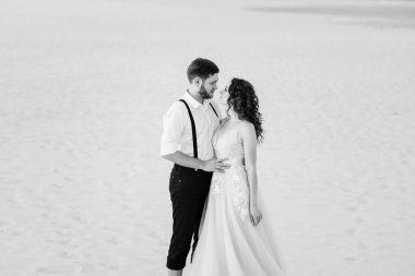 Genç çift, siyah pantolonlu bir adam ve pembe elbiseli bir kız çölün beyaz kumu boyunca yürüyorlar.