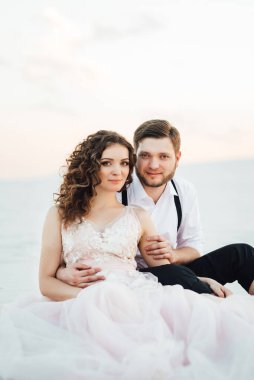 Genç çift, siyah pantolonlu bir adam ve pembe elbiseli bir kız çölün beyaz kumu boyunca yürüyorlar.