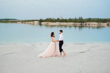 Genç çift, siyah pantolonlu bir adam ve pembe elbiseli bir kız çölün beyaz kumu boyunca yürüyorlar.