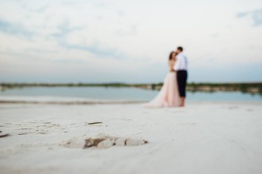 Genç çift, siyah pantolonlu bir adam ve pembe elbiseli bir kız çölün beyaz kumu boyunca yürüyorlar.