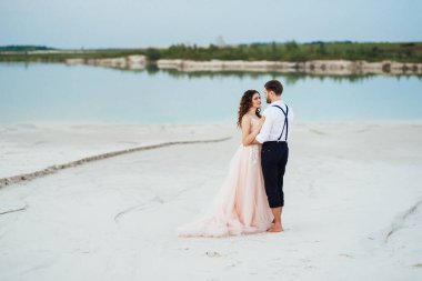 Genç çift, siyah pantolonlu bir adam ve pembe elbiseli bir kız çölün beyaz kumu boyunca yürüyorlar.