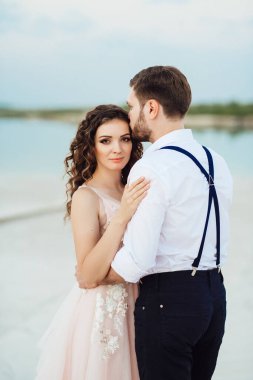 Genç çift, siyah pantolonlu bir adam ve pembe elbiseli bir kız çölün beyaz kumu boyunca yürüyorlar.