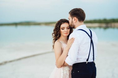 Genç çift, siyah pantolonlu bir adam ve pembe elbiseli bir kız çölün beyaz kumu boyunca yürüyorlar.