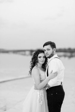 Genç çift, siyah pantolonlu bir adam ve pembe elbiseli bir kız çölün beyaz kumu boyunca yürüyorlar.