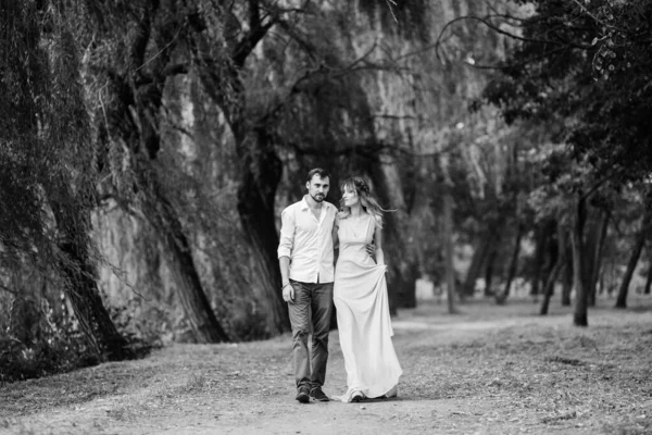 男と女が柳と森に覆われた川のほとりを歩いている — ストック写真