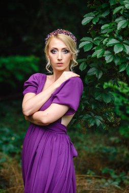 Yeşil ormanlı bir buketle leylak elbiseli manken sarışın kız.