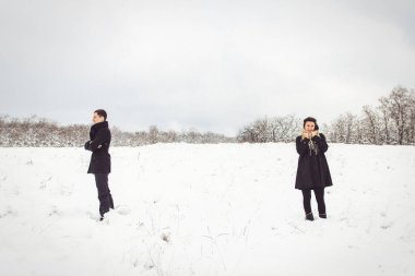Bir adam ve bir kız sıcak giysiler ve eşarplar içinde karlı ormanda ve tarlada yürüyüşe çıktılar.