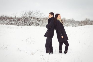 Bir adam ve bir kız sıcak giysiler ve eşarplar içinde karlı ormanda ve tarlada yürüyüşe çıktılar.