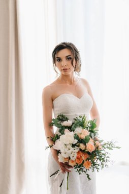 Beyaz elbiseli gelin ve otel odasında bir buket çiçek.