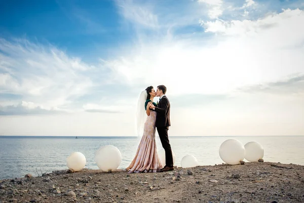 穿着棕色西服的新郎和穿着象牙衣服的新娘在岩石海岸 — 图库照片