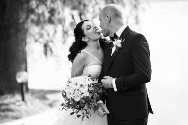 Beyaz elbiseli siyah saçlı bir gelin ve düğün günlerinde parkta papyonlu mavi elbiseli bir damat.