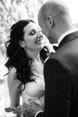 Beyaz elbiseli siyah saçlı bir gelin ve düğün günlerinde parkta papyonlu mavi elbiseli bir damat.