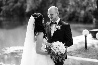 Beyaz elbiseli siyah saçlı bir gelin ve düğün günlerinde parkta papyonlu mavi elbiseli bir damat.