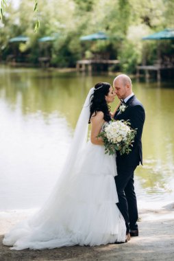 Beyaz elbiseli siyah saçlı bir gelin ve düğün günlerinde parkta papyonlu mavi elbiseli bir damat.