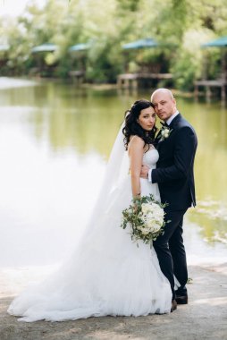 Beyaz elbiseli siyah saçlı bir gelin ve düğün günlerinde parkta papyonlu mavi elbiseli bir damat.