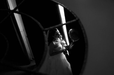 Beyaz elbiseli siyah saçlı bir gelin ve koyu renk bir otel odasında papyonlu mavi takım elbiseli bir damat.