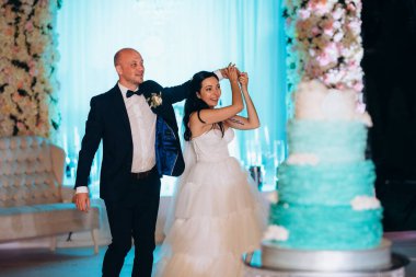 Yeni evliler mutlu bir şekilde kesiyor, gülüyor ve mavi düğün pastasını tadıyor.