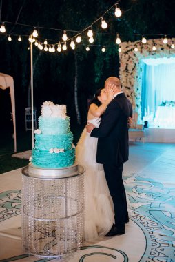Yeni evliler mutlu bir şekilde kesiyor, gülüyor ve mavi düğün pastasını tadıyor.