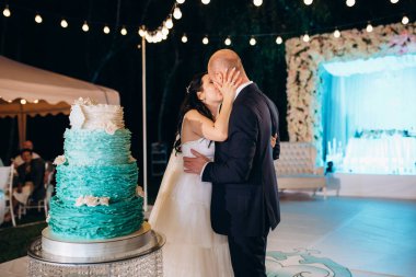 Yeni evliler mutlu bir şekilde kesiyor, gülüyor ve mavi düğün pastasını tadıyor.