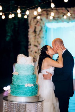 Yeni evliler mutlu bir şekilde kesiyor, gülüyor ve mavi düğün pastasını tadıyor.