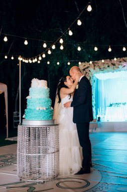 Yeni evliler mutlu bir şekilde kesiyor, gülüyor ve mavi düğün pastasını tadıyor.