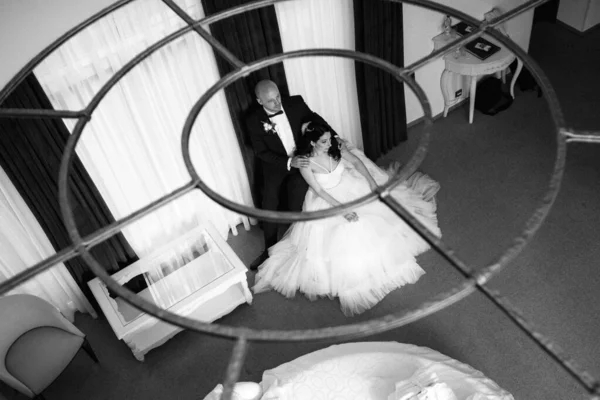 Beyaz elbiseli siyah saçlı bir gelin ve koyu renk bir otel odasında papyonlu mavi takım elbiseli bir damat.