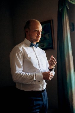 Evin içinde ve dışarıda mavi takım elbiseli ve papyonlu genç bir damadın portresi.