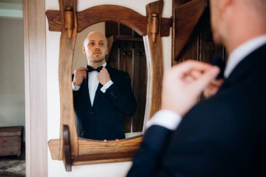 Evin içinde ve dışarıda mavi takım elbiseli ve papyonlu genç bir damadın portresi.