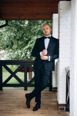 Evin içinde ve dışarıda mavi takım elbiseli ve papyonlu genç bir damadın portresi.