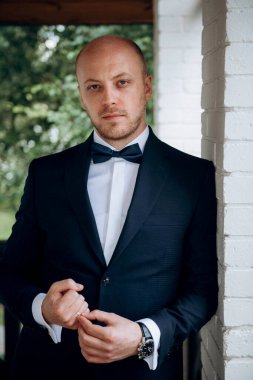 Evin içinde ve dışarıda mavi takım elbiseli ve papyonlu genç bir damadın portresi.