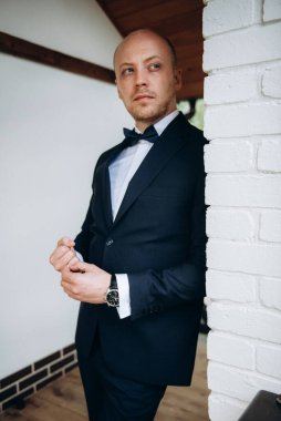 Evin içinde ve dışarıda mavi takım elbiseli ve papyonlu genç bir damadın portresi.