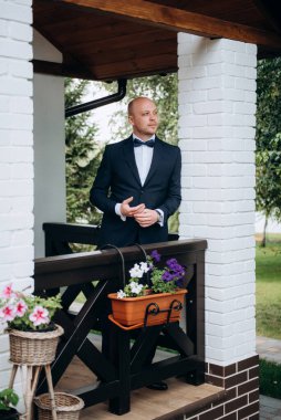 Evin içinde ve dışarıda mavi takım elbiseli ve papyonlu genç bir damadın portresi.