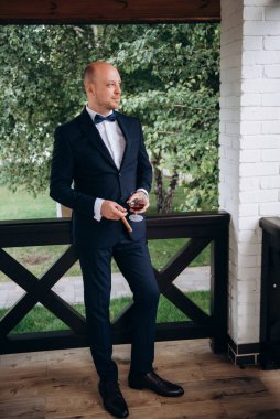 Evin içinde ve dışarıda mavi takım elbiseli ve papyonlu genç bir damadın portresi.