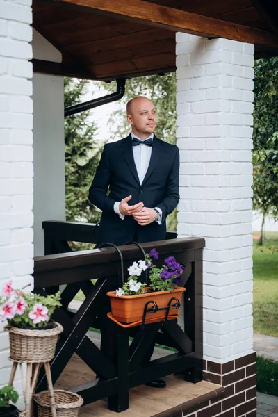 Evin içinde ve dışarıda mavi takım elbiseli ve papyonlu genç bir damadın portresi.