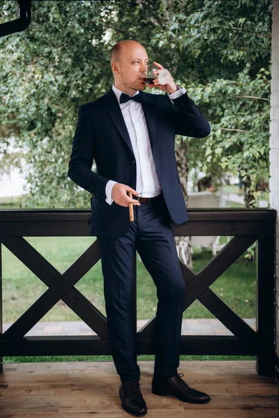 Evin içinde ve dışarıda mavi takım elbiseli ve papyonlu genç bir damadın portresi.