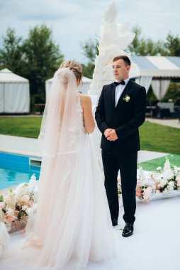 Gelin ve damadın bir restoranda düğün töreni. Beyaz kanatların ve mavi bir havuzun önünde.