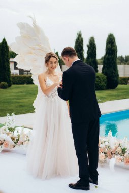 Gelin ve damadın bir restoranda düğün töreni. Beyaz kanatların ve mavi bir havuzun önünde.