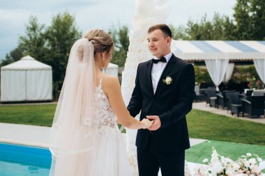 Gelin ve damadın bir restoranda düğün töreni. Beyaz kanatların ve mavi bir havuzun önünde.