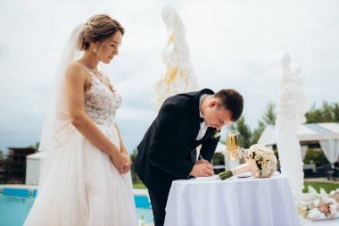 Gelin ve damadın bir restoranda düğün töreni. Beyaz kanatların ve mavi bir havuzun önünde.