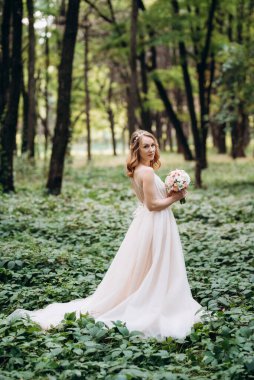 Yeşil bir bahar ormanında açık mercan elbiseli sarışın gelin.