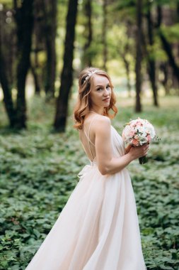 Yeşil bir bahar ormanında açık mercan elbiseli sarışın gelin.