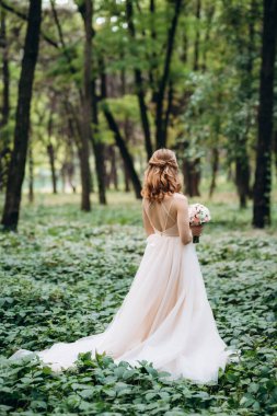 Yeşil bir bahar ormanında açık mercan elbiseli sarışın gelin.