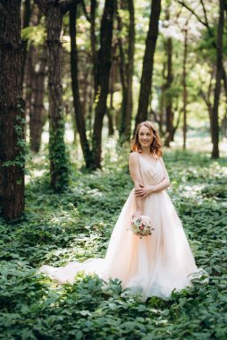 Yeşil bir bahar ormanında açık mercan elbiseli sarışın gelin.
