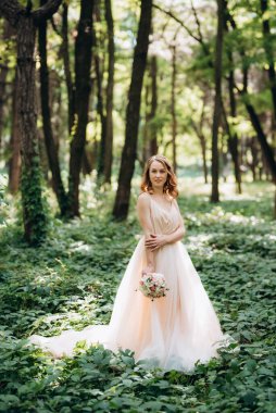Yeşil bir bahar ormanında açık mercan elbiseli sarışın gelin.