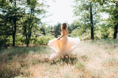 Yeşil bir bahar ormanında açık mercan elbiseli sarışın gelin.