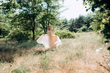 Yeşil bir bahar ormanında açık mercan elbiseli sarışın gelin.